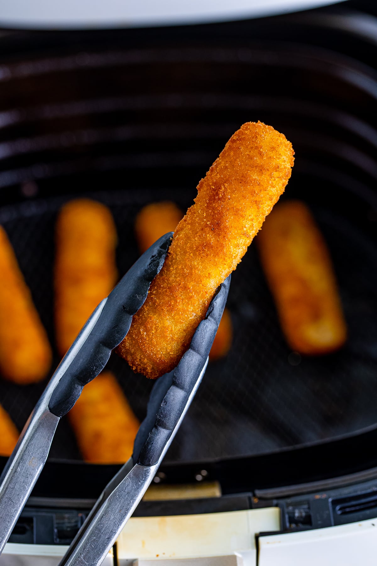 air fryer fish sticks being held up with tongs in air