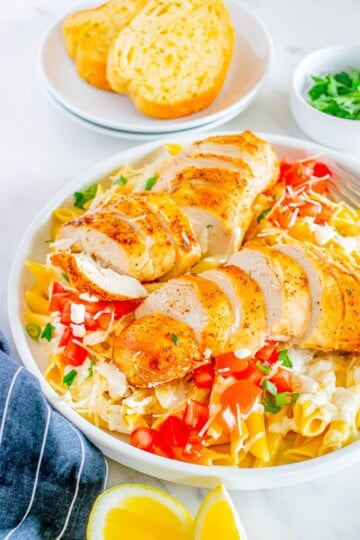 A white bowl of Cajun Chicken Pasta topped with sliced cajun chicken, diced tomatoes, green onions, and shredded Parmesan.