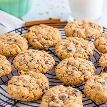 Stack of Soft Chewy Old Fashioned Oatmeal Raisin Cookies on a parchment-lined surface with cinnamon sticks and scattered oats.