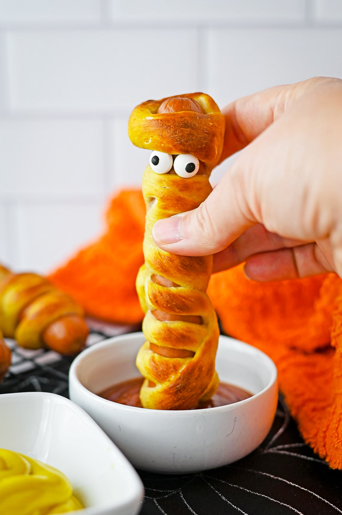 a pretzel dog being dipped into ketchup by hand