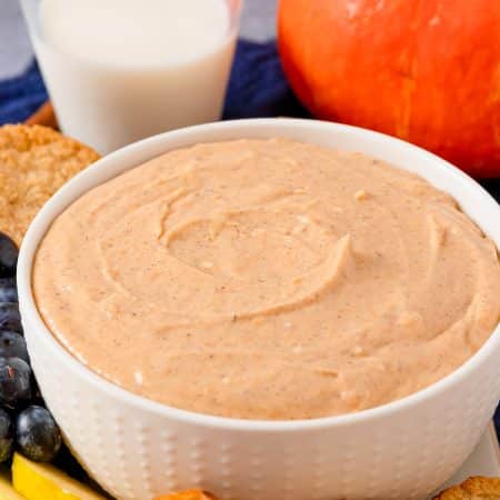 A bowl of creamy pumpkin dip surrounded by apple slices, pretzels, and cookies for dipping.