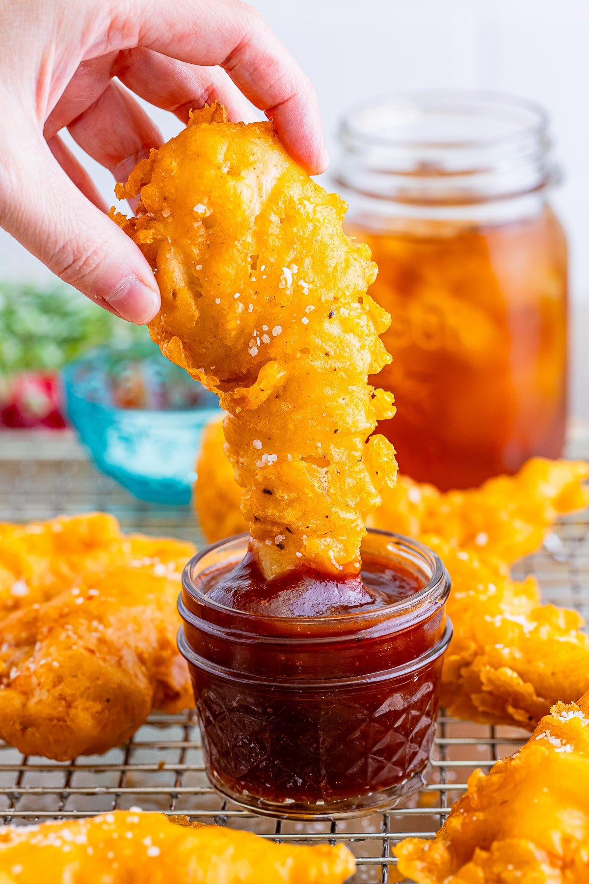 a hand dipping battered chicken tenders into bbq sauce