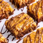German chocolate brownies topped with coconut pecan frosting and chocolate drizzle cut into squares.