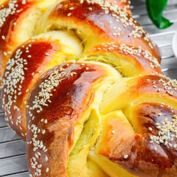 A golden braided challah bread loaf topped with sesame seeds.
