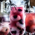 Halloween Punch in a glass with longan and blueberry eyeballs, a plastic spider, and spooky smoke behind it.