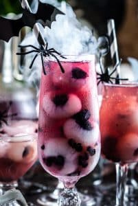 Halloween Punch in a glass with longan and blueberry eyeballs, a plastic spider, and spooky smoke behind it.