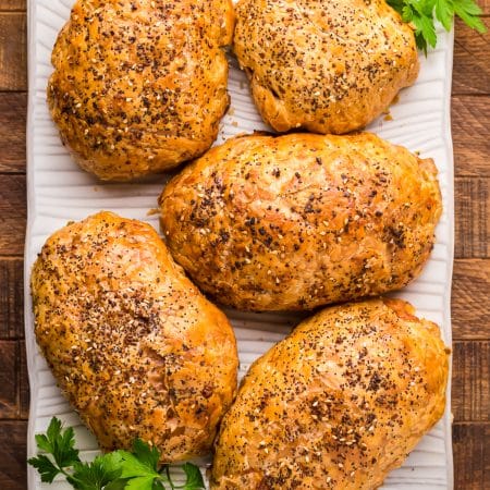 Four golden chicken in puff pastry packages on a wooden board garnished with parsley.