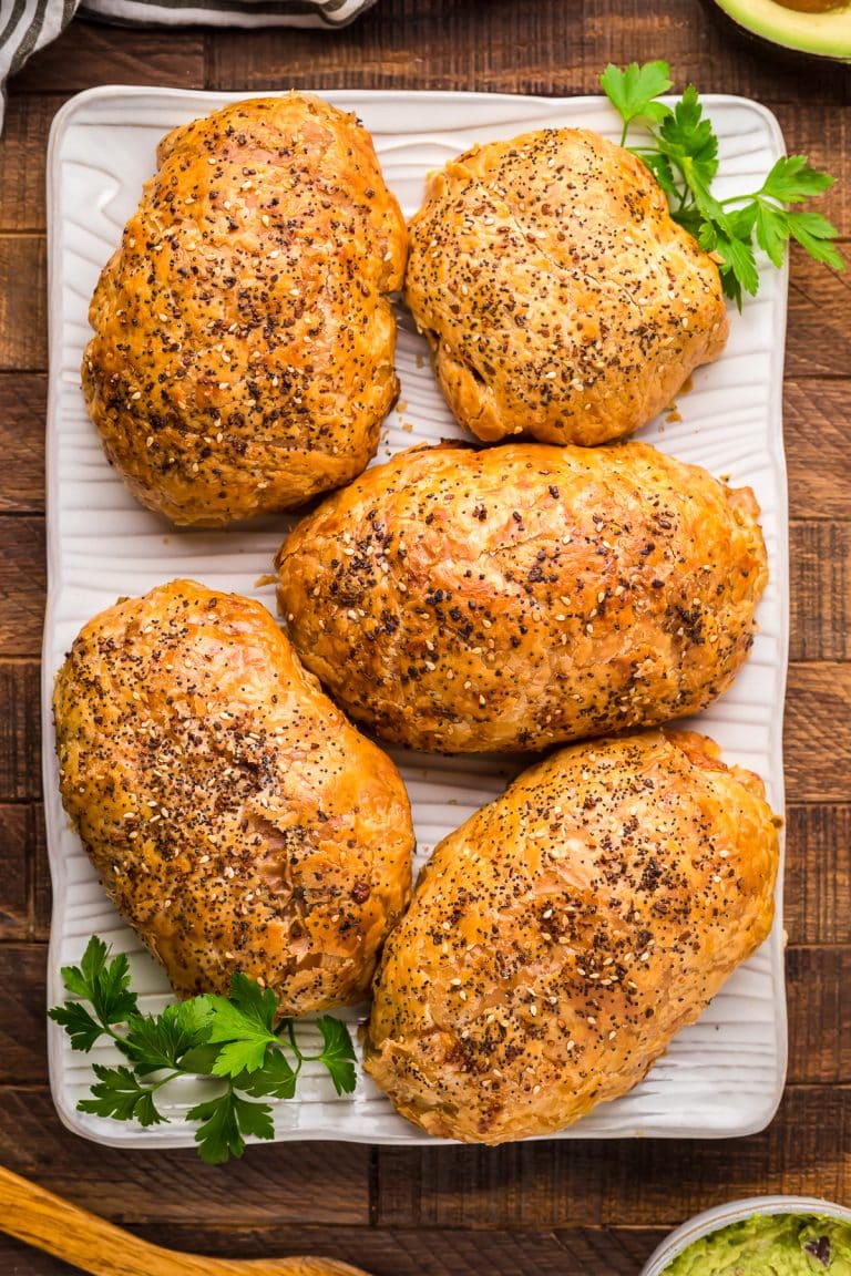 Four golden chicken in puff pastry packages on a wooden board garnished with parsley.