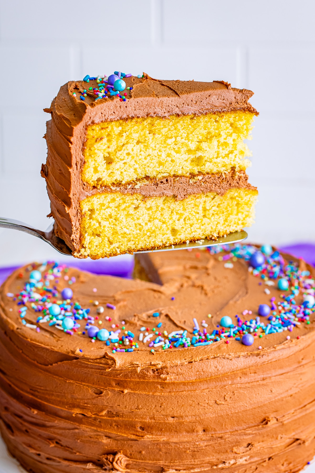 cake server holding up a slice of yellow cake with chocolate frosting in air