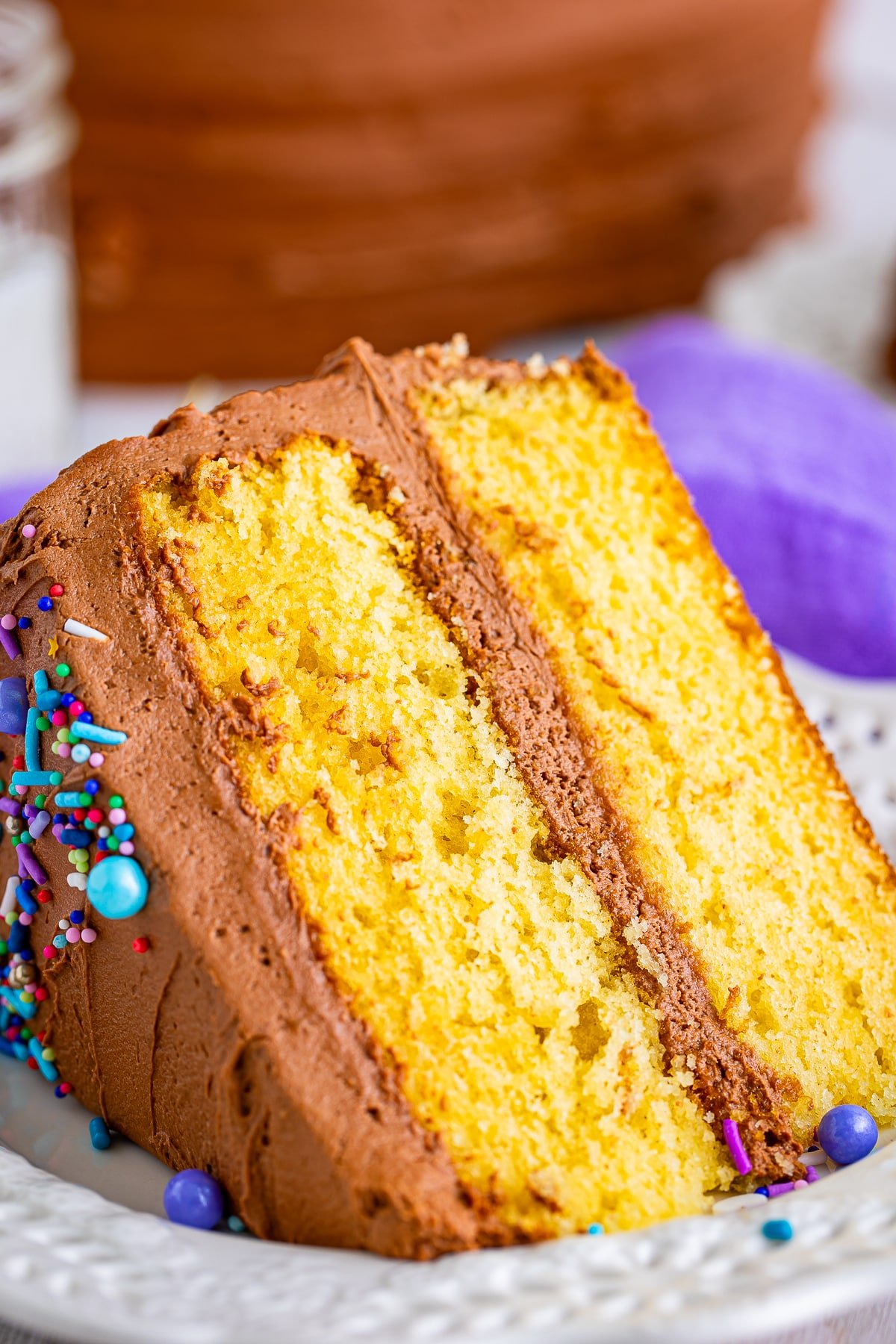 close up of a slice of yellow cake with chocolate frosting on a plate