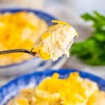 A spoonful of ultra creamy cheesy grits lifted from a bowl topped with melted cheddar.