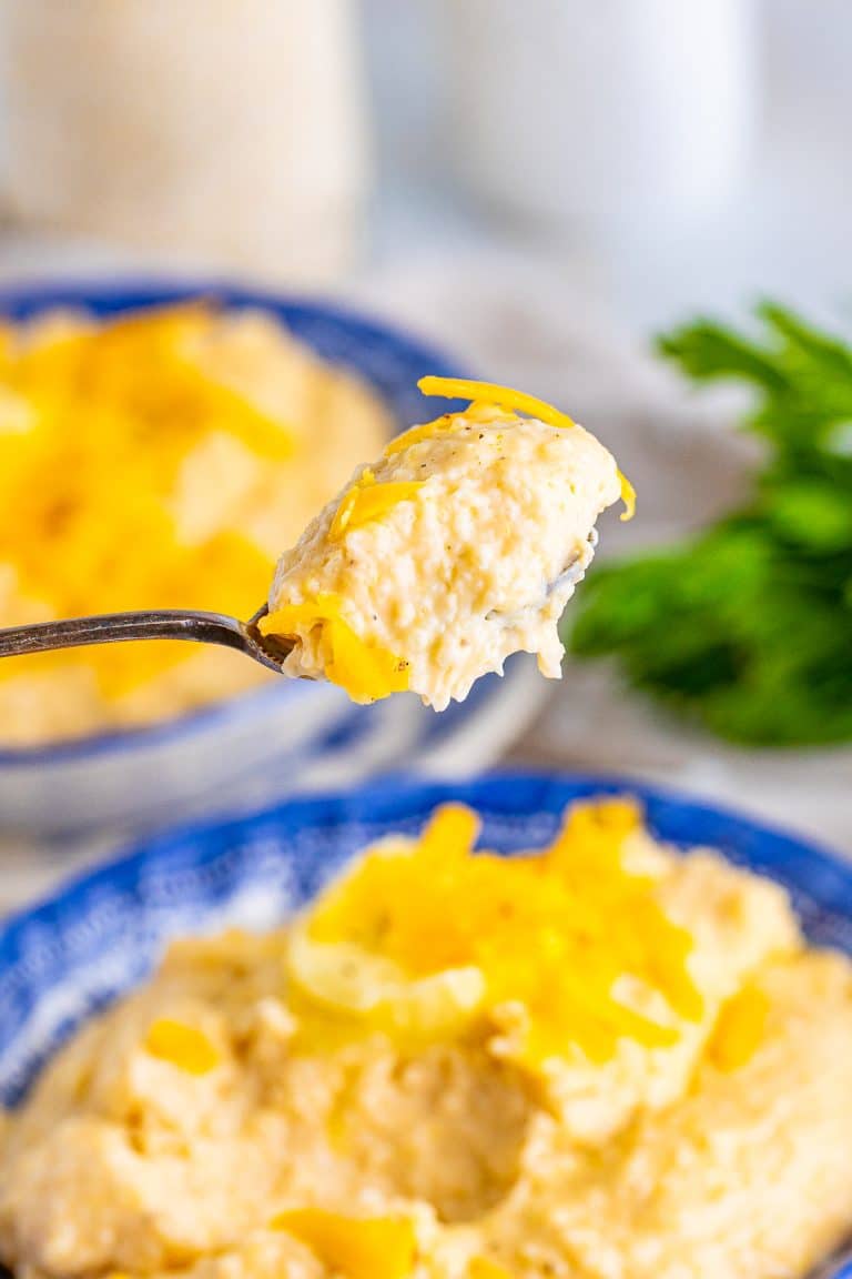 A spoonful of ultra creamy cheesy grits lifted from a bowl topped with melted cheddar.
