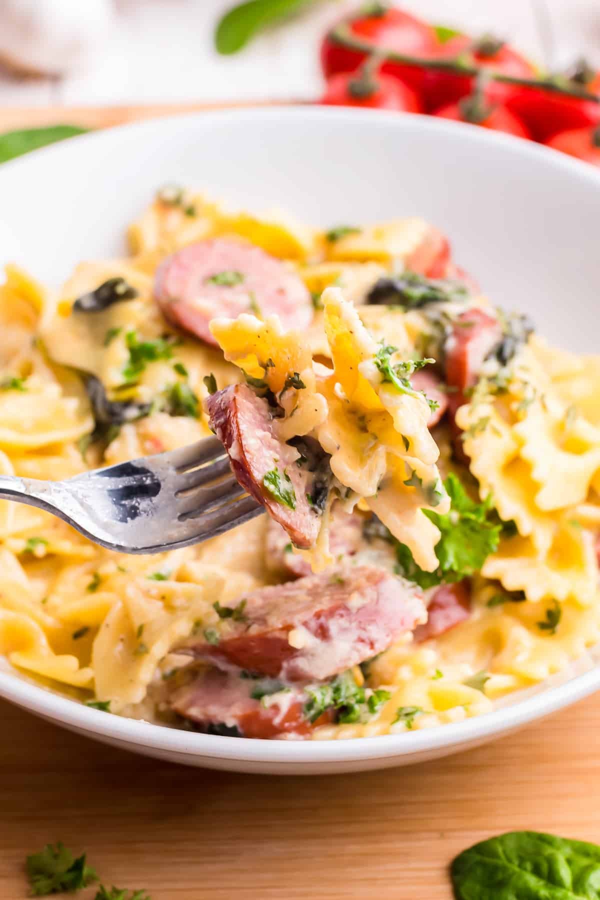 a fork holding up a bite of creamy sausage pasta in air