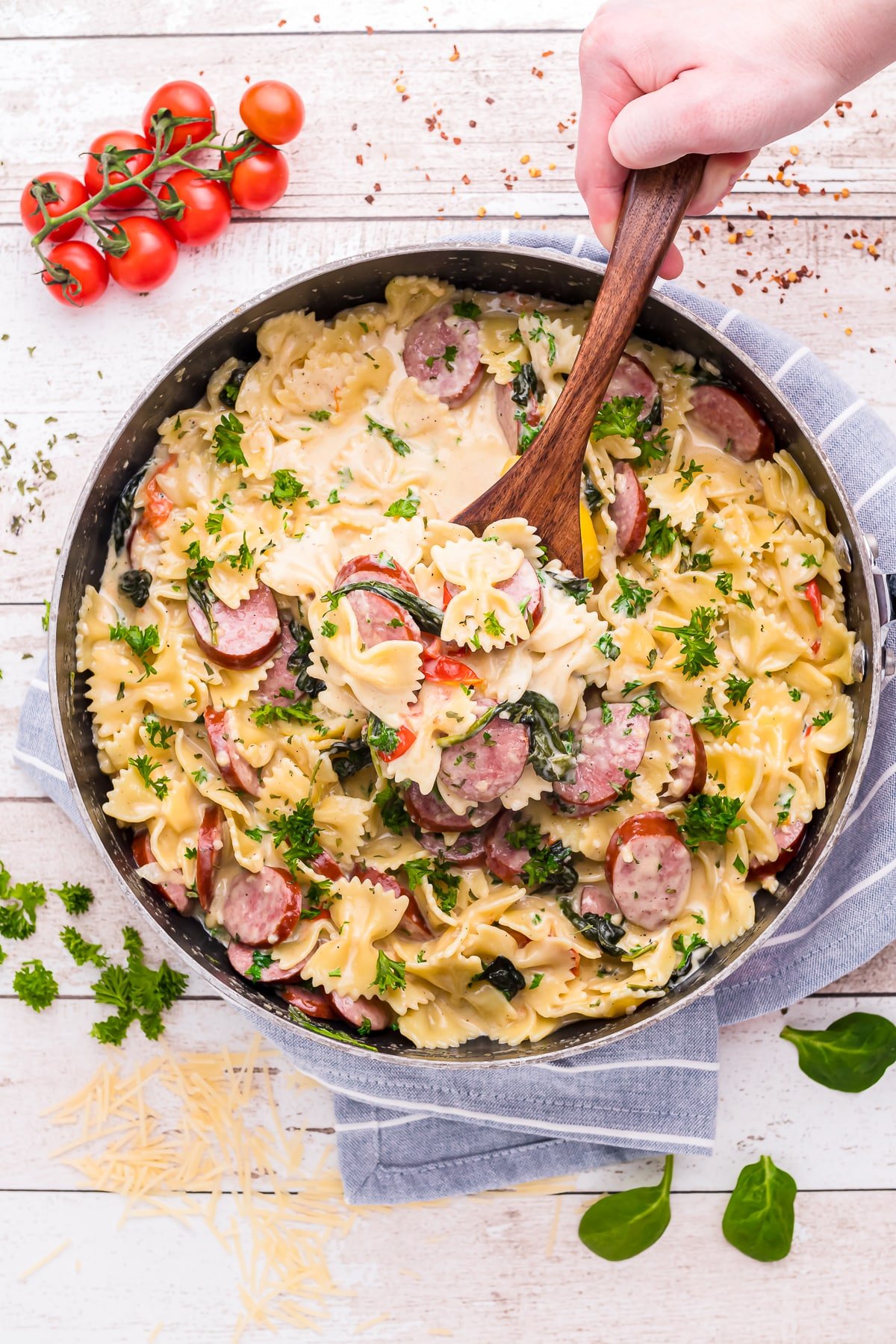 a hand scooping out creamy sausage pasta from pot
