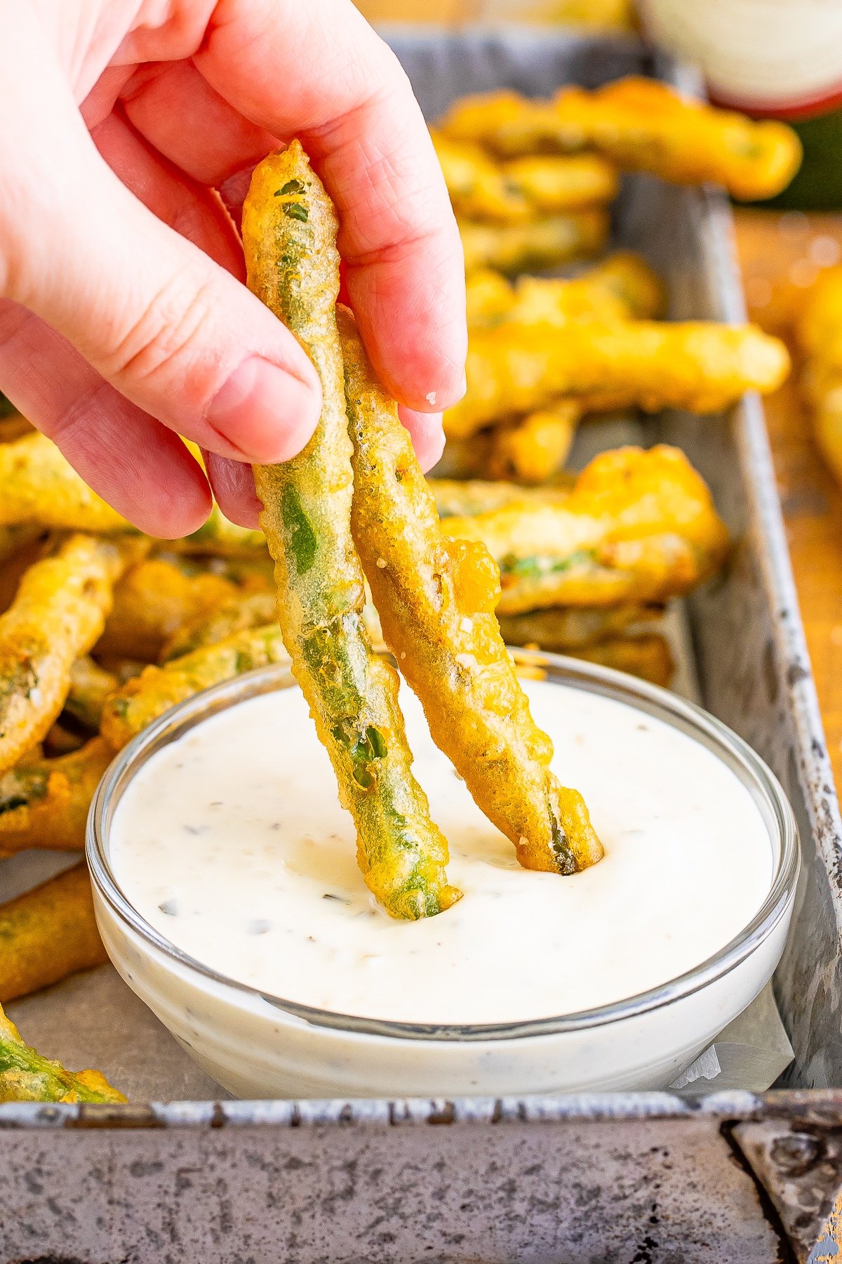 a hand dipping fried green beans recipe into ranch