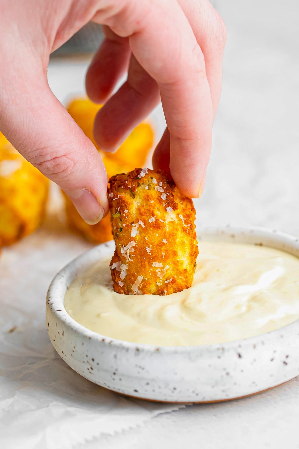 a hand dipping air fry tater tots in dipping sauce