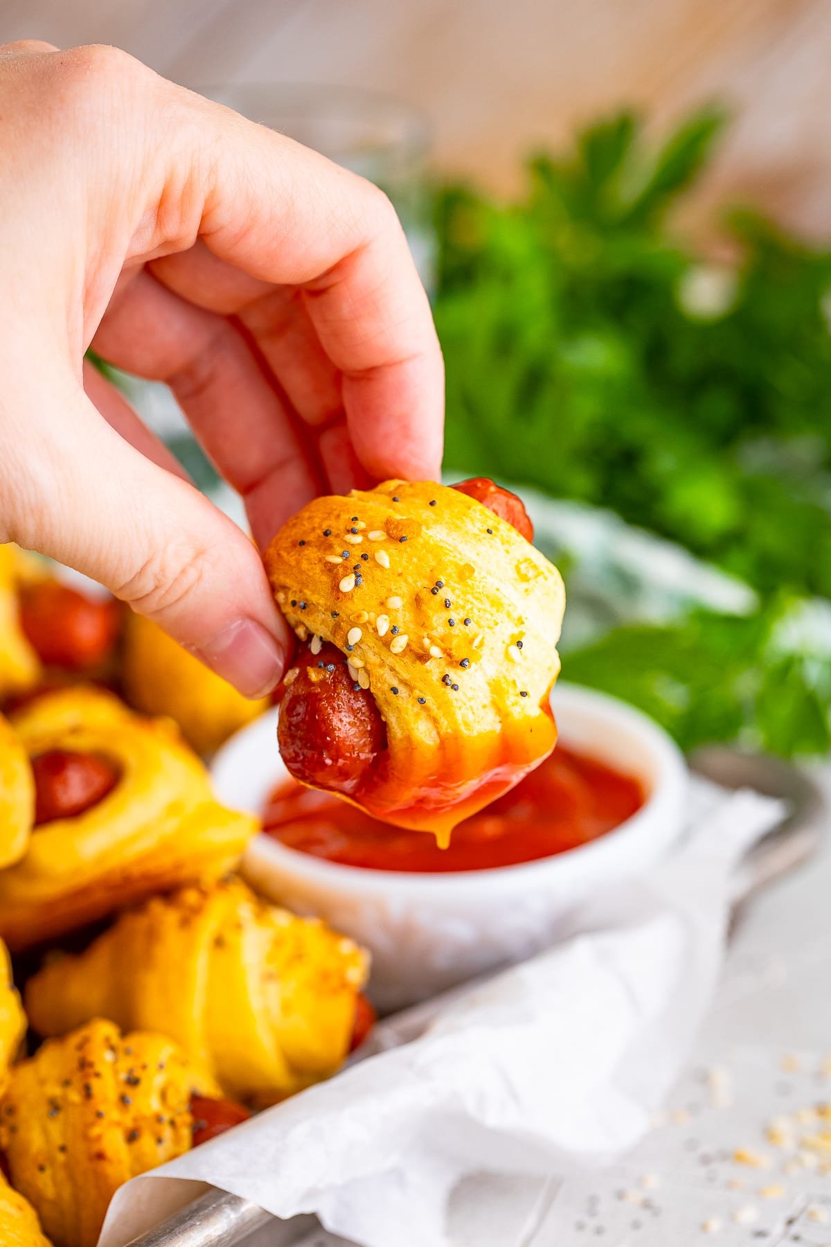 hand holding up mini pigs in a blanket that has been dipped in ketchup
