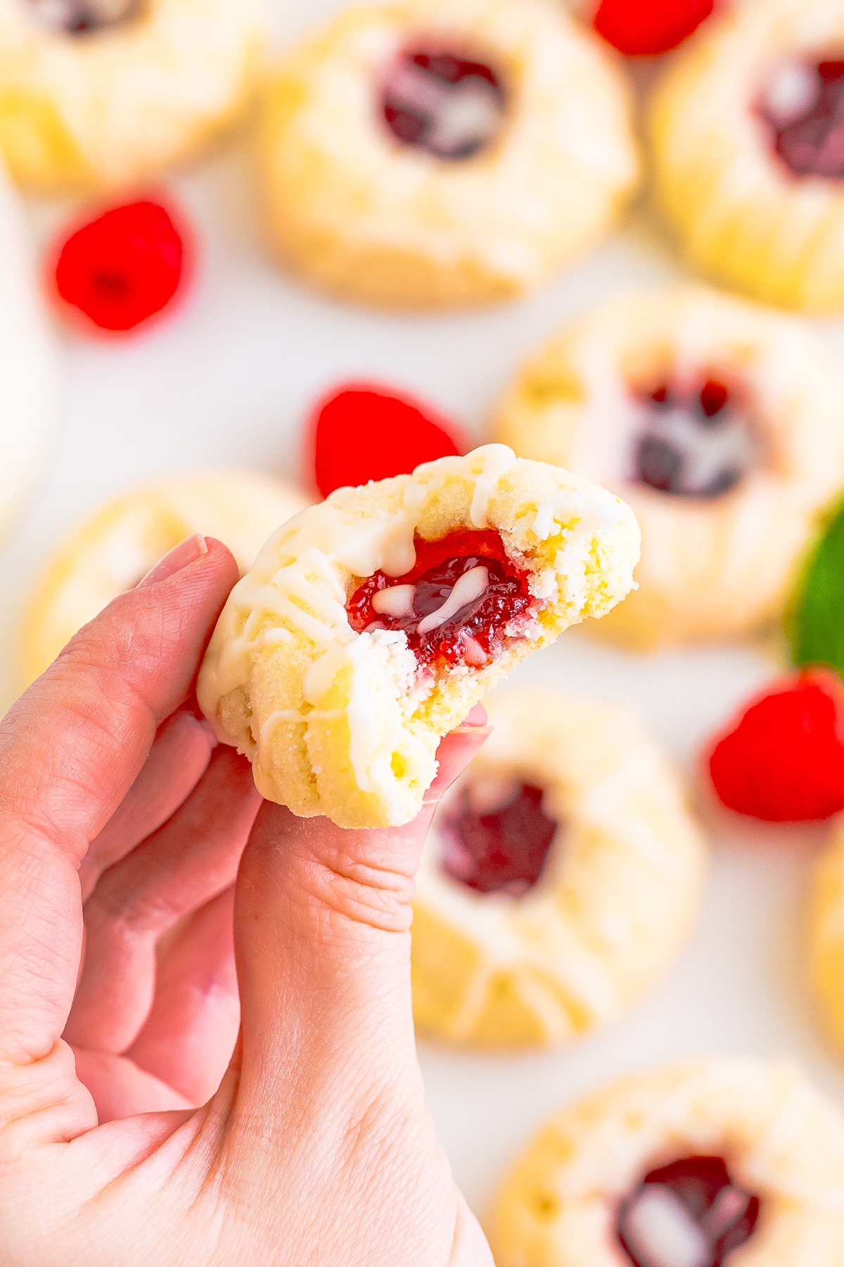 a hand holding up a raspberry thumbprint cookie with a bite taken out