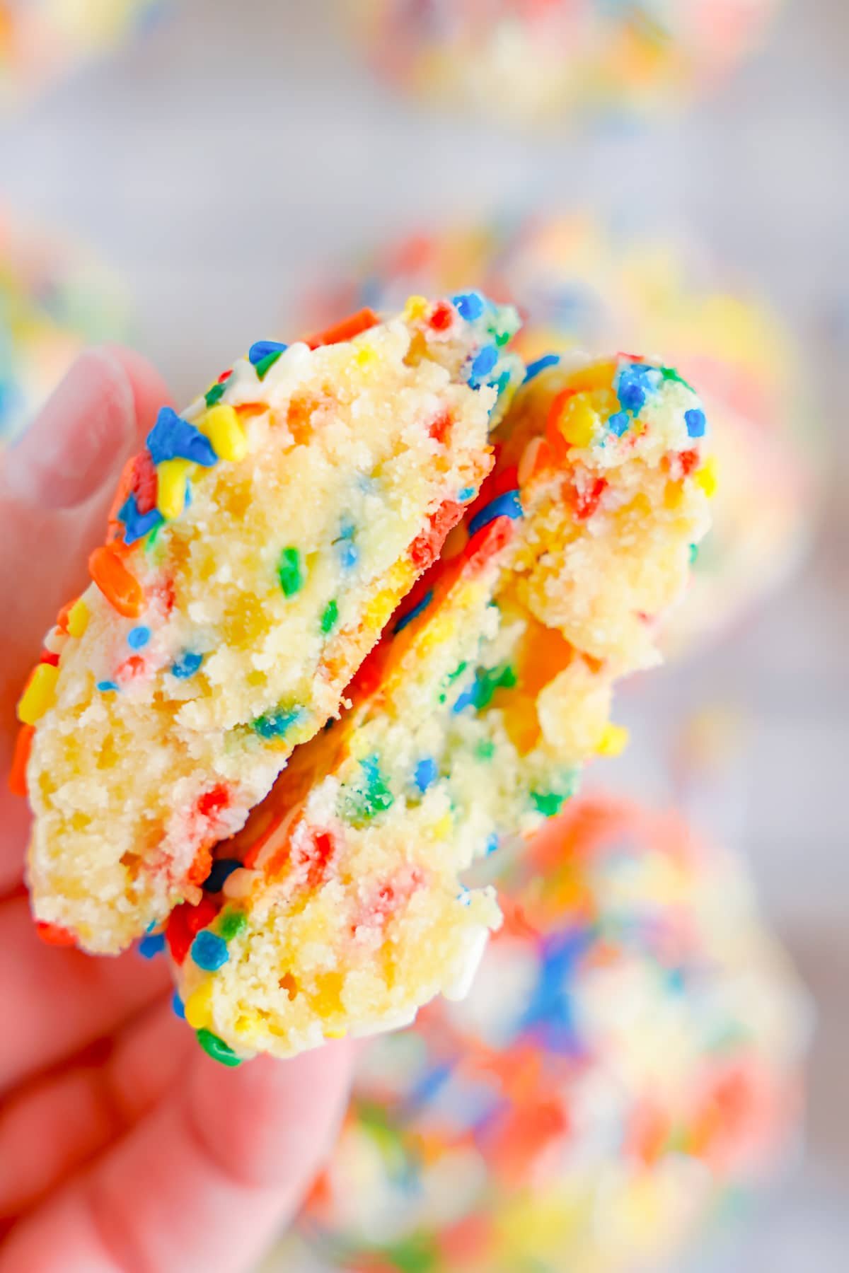 a hand holding up sprinkle cookies to see the interior