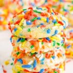 A tall stack of Sprinkle Cookies coated in colorful rainbow sprinkles on a white surface.
