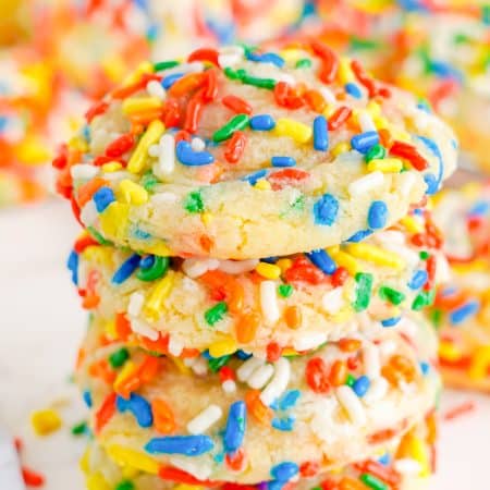 A tall stack of Sprinkle Cookies coated in colorful rainbow sprinkles on a white surface.