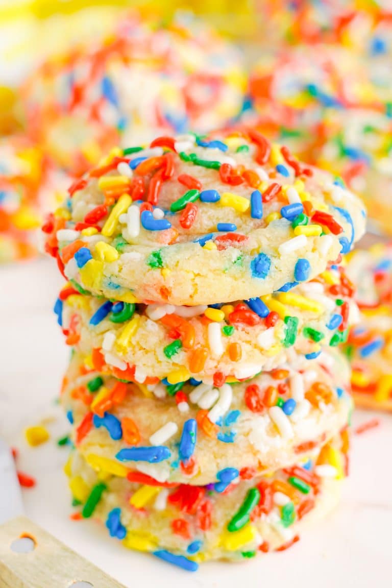 A tall stack of Sprinkle Cookies coated in colorful rainbow sprinkles on a white surface.