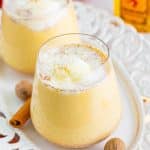 A glass of creamy Christmas punch topped with a scoop of vanilla ice cream and grated nutmeg on a white plate.