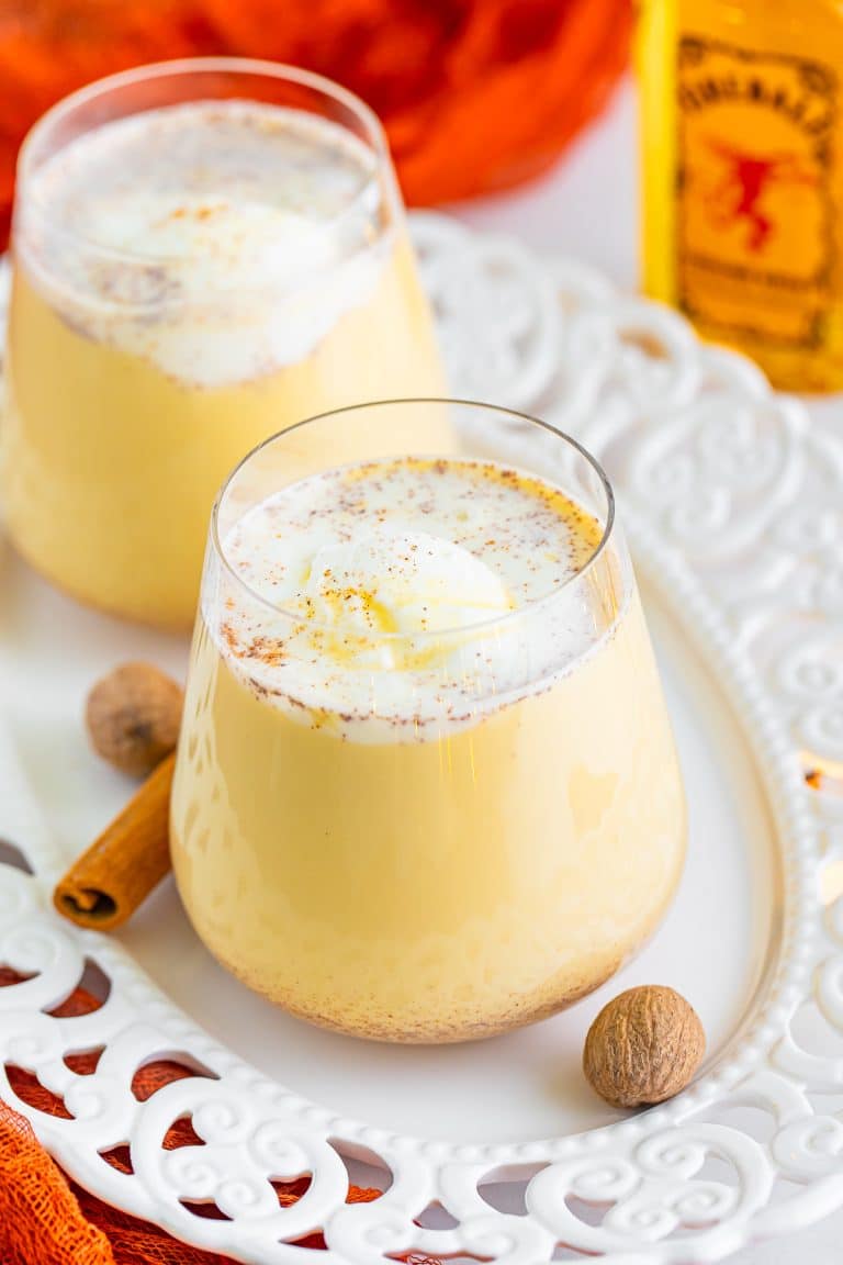 A glass of creamy Christmas punch topped with a scoop of vanilla ice cream and grated nutmeg on a white plate.