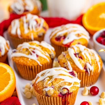 Glazed Cranberry Orange Muffins on a white platter with a fresh orange and red linen.