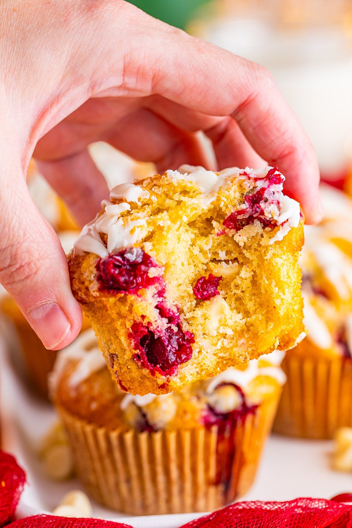 a hand holding up orange cranberry muffins with a bite taken out in air