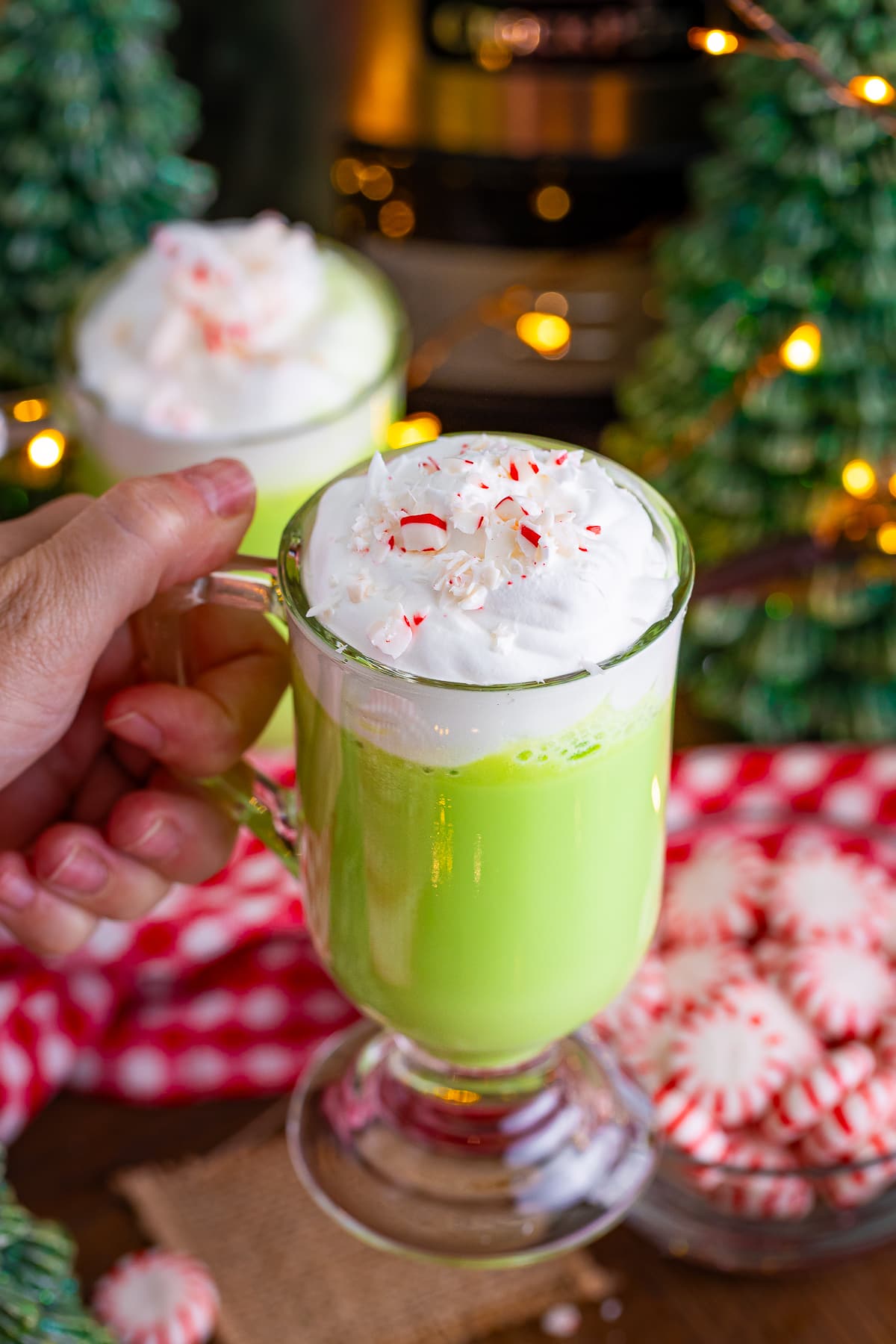a hand holding up a mug of grinch hot cocoa