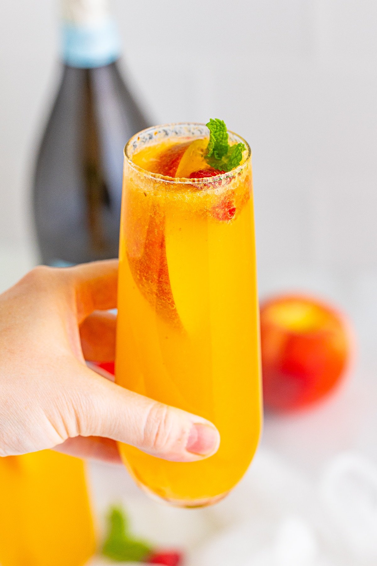 peach bellini recipe in a glass being held in air by a hand