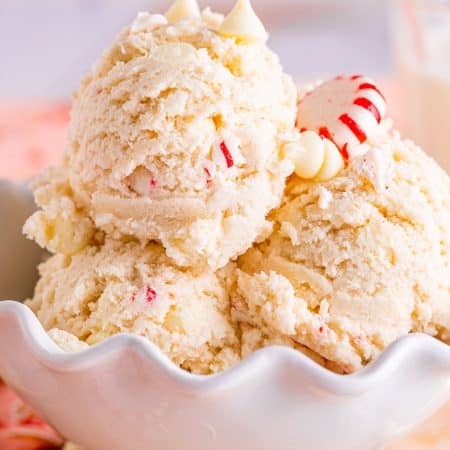 Edible sugar cookie dough scooped into a white bowl with white chocolate chips and peppermint candies.
