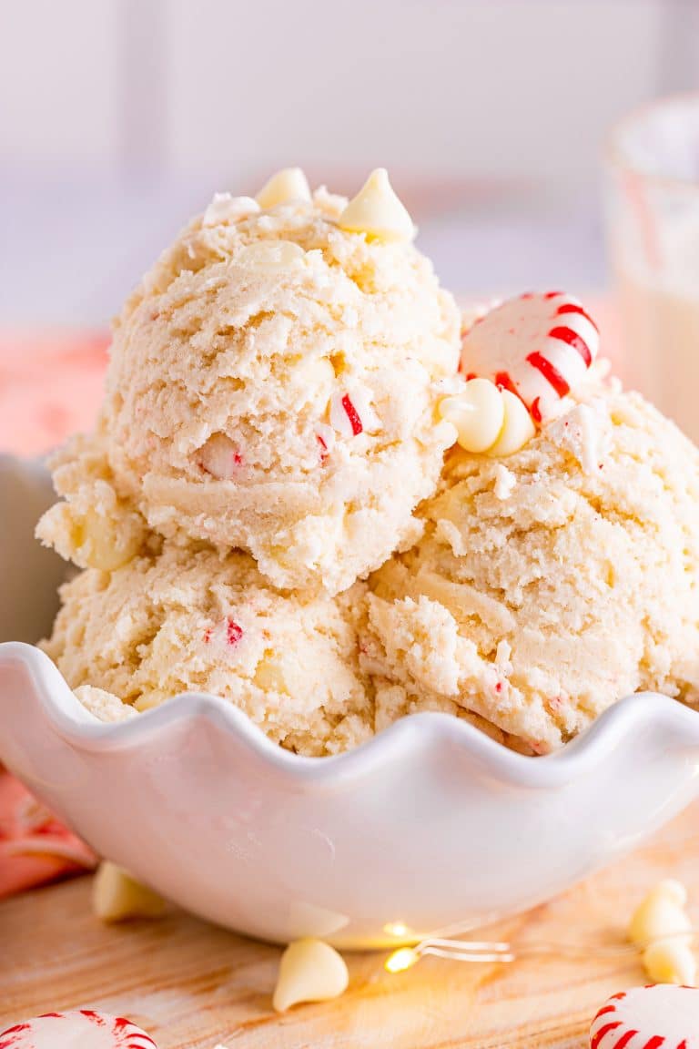 Edible sugar cookie dough scooped into a white bowl with white chocolate chips and peppermint candies.