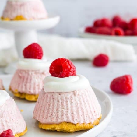 A mini lemon cheesecake topped with whipped topping and a fresh raspberry on a white plate.