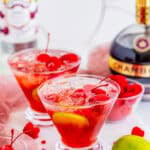 Two love potion cocktails in martini glasses garnished with cherries and lime wheels.