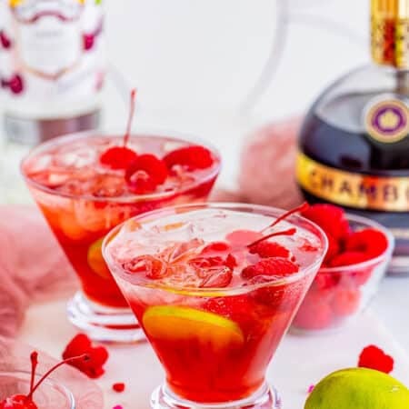 Two love potion cocktails in martini glasses garnished with cherries and lime wheels.