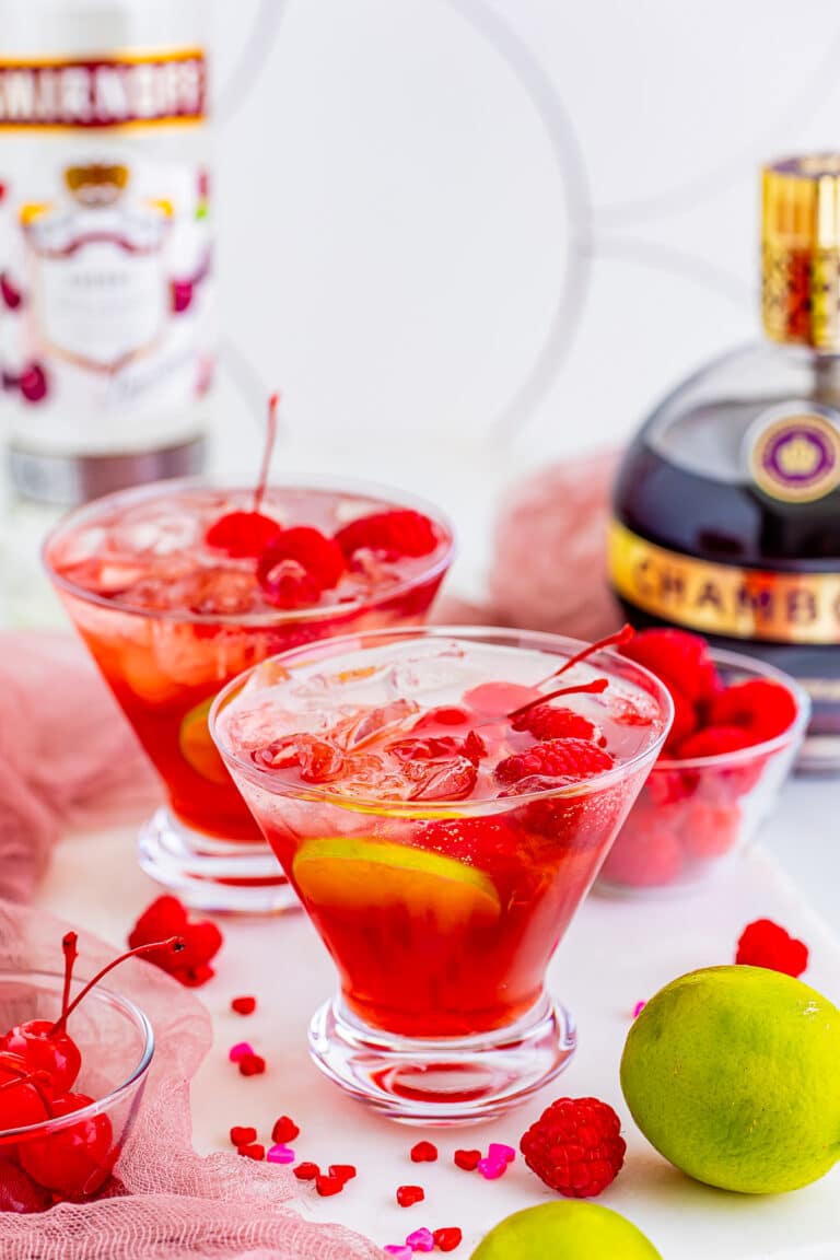 Two love potion cocktails in martini glasses garnished with cherries and lime wheels.