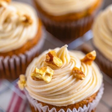 A banana cupcake topped with a tall swirl of cream cheese frosting and candied walnuts.