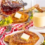 Maple syrup being poured over a plate of eggnog french toast topped with butter.
