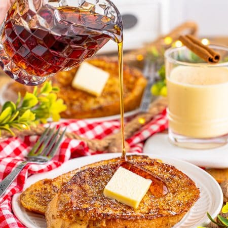 Maple syrup being poured over a plate of eggnog french toast topped with butter.