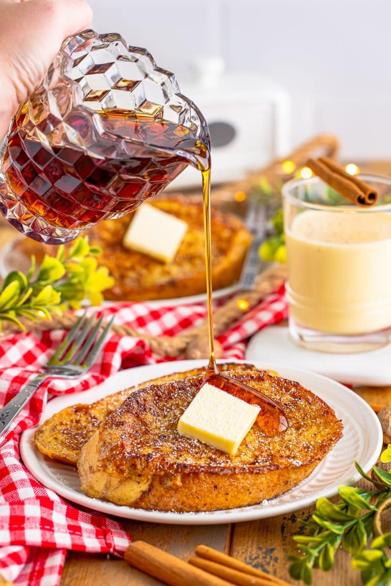Maple syrup being poured over a plate of eggnog french toast topped with butter.