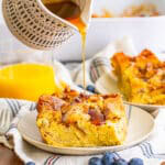 A slice of overnight french toast casserole on a plate with berries and maple syrup.