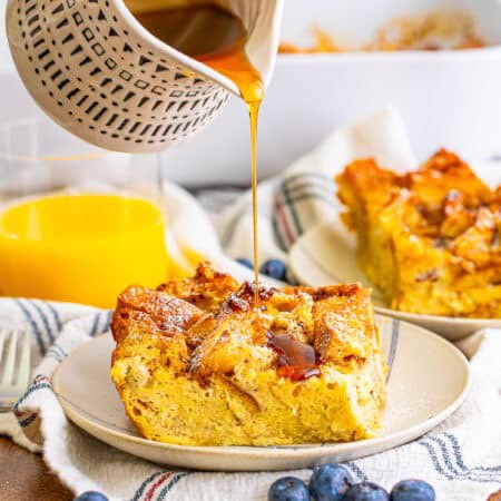 A slice of overnight french toast casserole on a plate with berries and maple syrup.