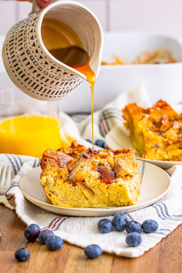 A slice of overnight french toast casserole on a plate with berries and maple syrup.