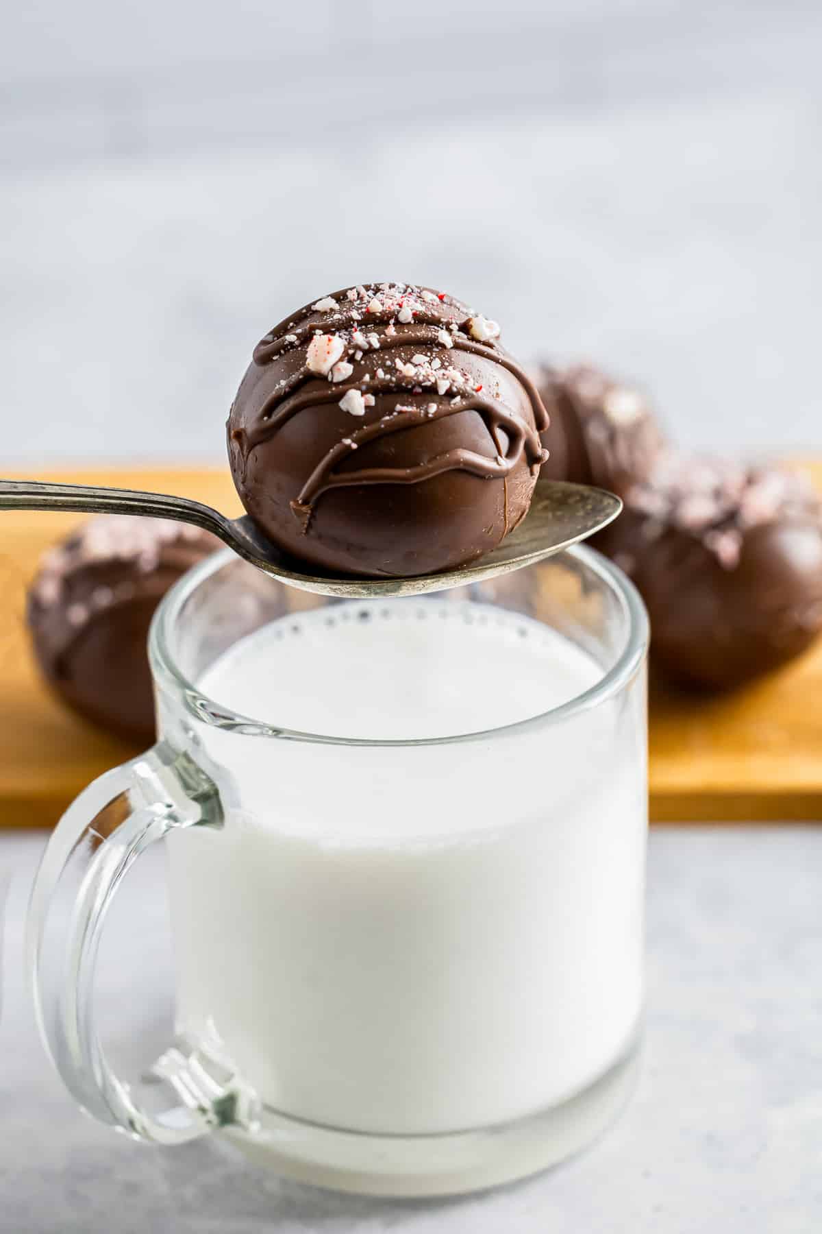 a spoon holding a hot cocoa bombs recipe over a mug of milk