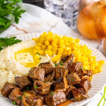 A plate of slow cooker steak bites with mashed potatoes and corn.