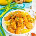A plate of sticky asian lemon chicken over rice garnished with green onions.