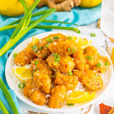 A plate of sticky asian lemon chicken over rice garnished with green onions.