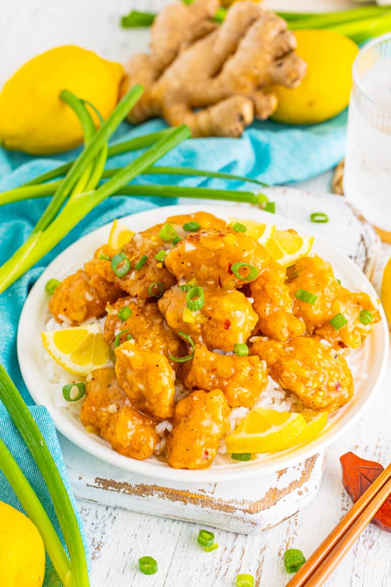 A plate of sticky asian lemon chicken over rice garnished with green onions.